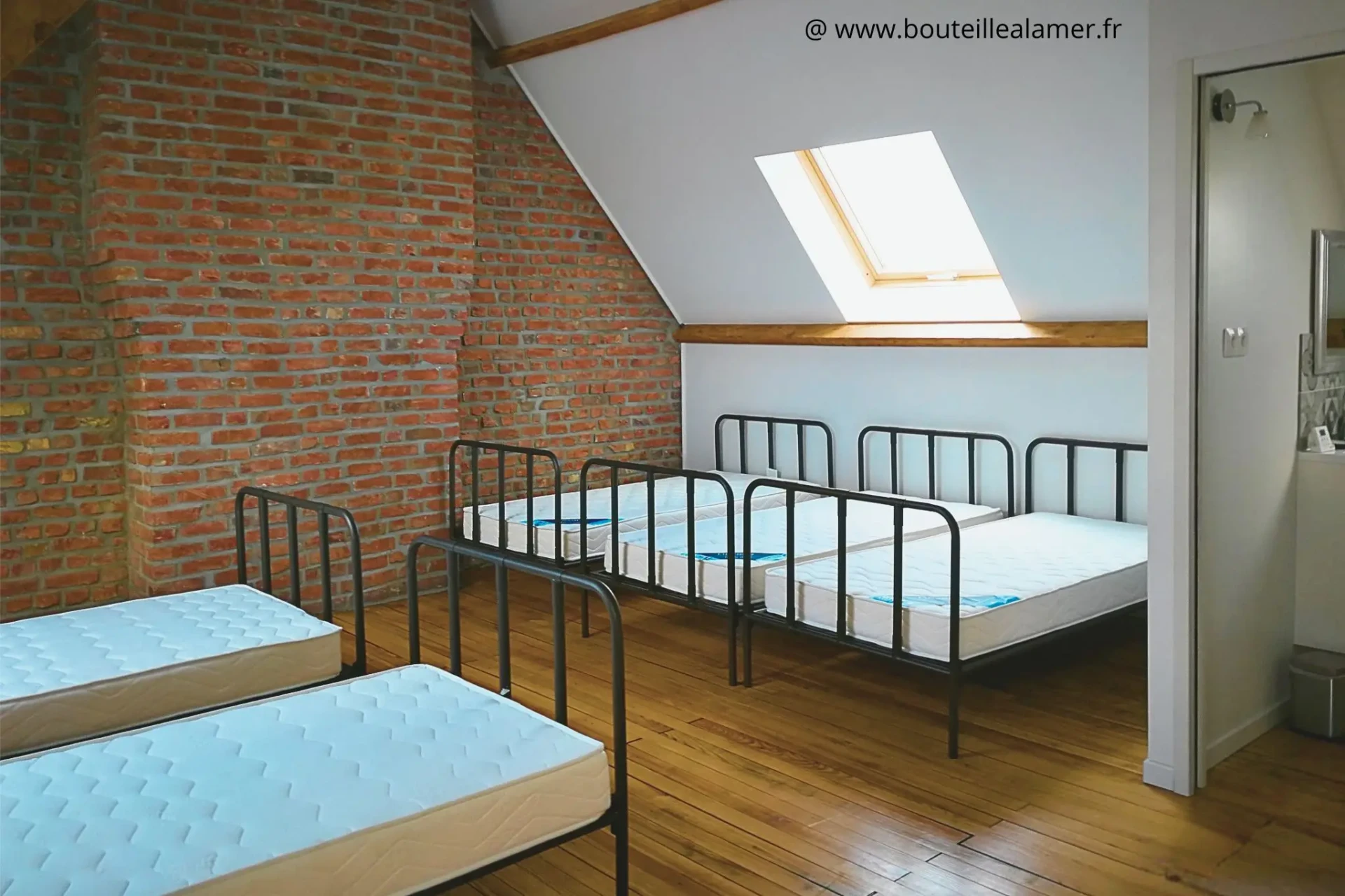 Dortoir spacieux avec cinq lits simples, poutres en bois apparentes, lumière naturelle, salle de bain privative et toilettes à l’étage, gîte Bouteille à la Mer, Côte d’Opale, Gravelines.